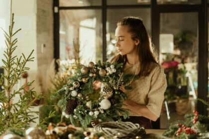 Woman crafting Christmas wreath with ornaments in cozy indoor setting. Perfect holiday season decor image.