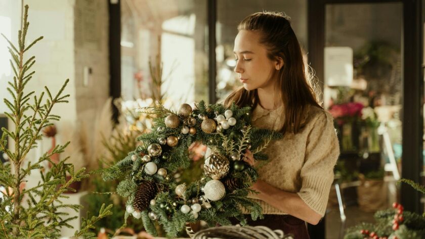 Woman crafting Christmas wreath with ornaments in cozy indoor setting. Perfect holiday season decor image.