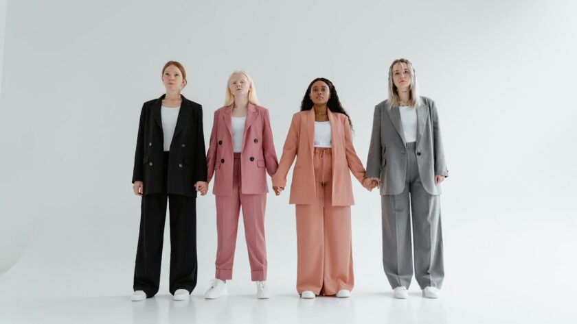 Group of four women in business suits holding hands, symbolizing diversity and equality.