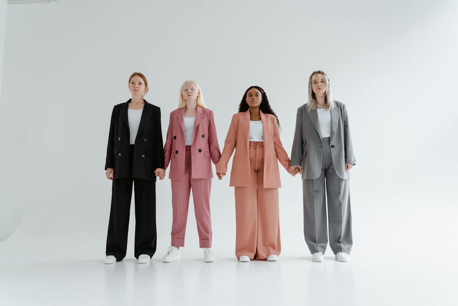 Group of four women in business suits holding hands, symbolizing diversity and equality.