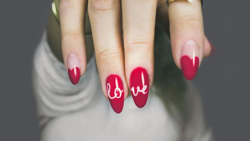 Vibrant red nails with 'love' art on a woman's hand, showcasing elegant style and design.