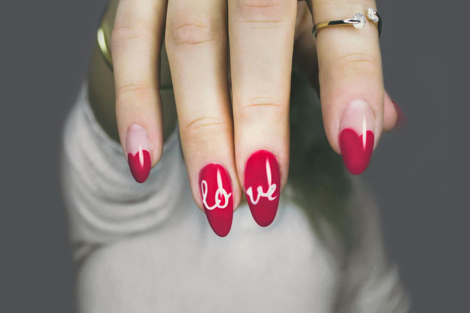 Vibrant red nails with 'love' art on a woman's hand, showcasing elegant style and design.