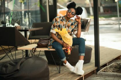 Trendy woman with sunglasses and flowers relaxing on a patio bench in sunlight.