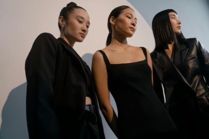 Three stylish women posing in chic black outfits against a minimalist backdrop.